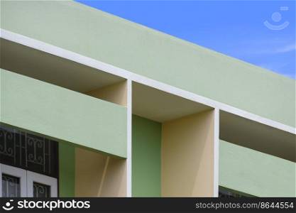 Abstract geometric pattern of shading fin concrete on modern green and beige building wall against blue sky background