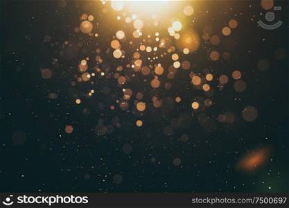 Abstract glittering gold with bokeh and dust effect . Black background .