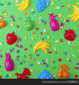 Abstract green background with childrens plastic toys and wooden multicolored letters, top view