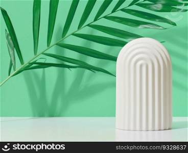 Abstract green background with white decorative arch and palm leaf and shadow, stage for showcasing products, cosmetics