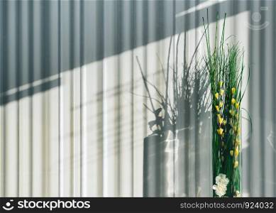 Abstract interior template - floor vase with floral decorations on a background of a striped wall with sunlight shadow.