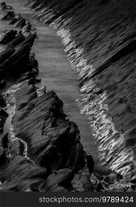 Abstract landscape image of rocks on Welcome Mouth Beach at sunset with tide marks on rocks reflecting sunlight