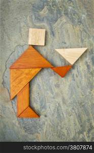 abstract of a butler, waiter or servant figure built from seven tangram wooden pieces, a traditional Chinese puzzle game; slate rock background, the artwork copyright by the photographer