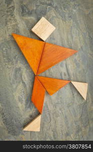 abstract of a dancing, running or walking figure built from seven tangram wooden pieces, a traditional Chinese puzzle game; slate rock background background, the artwork copyright by the photographer
