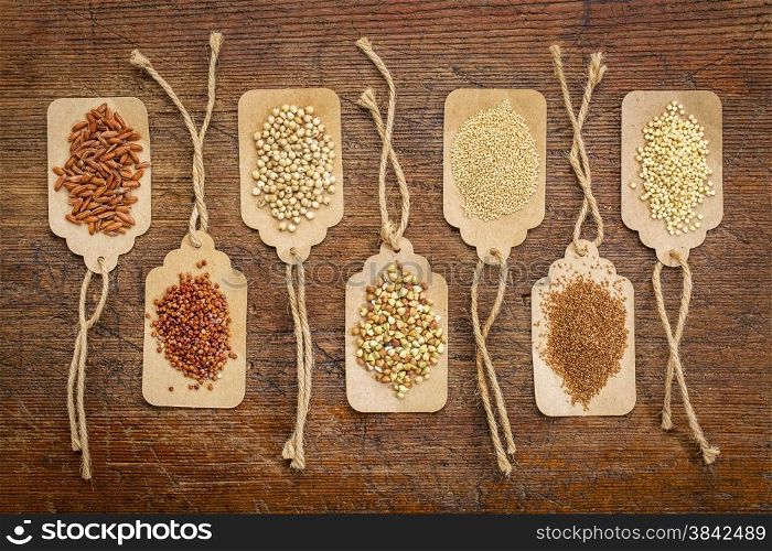 abstract of healthy, gluten free grains (quinoa, sorghum, brown rice, teff, buckwheat, amaranth, millet) - top view of paper price tags against rustic wood