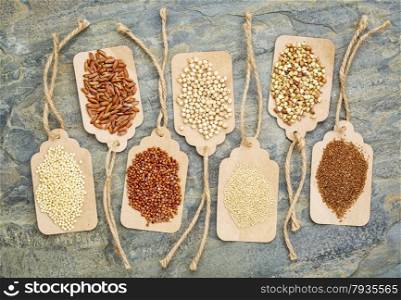 abstract of healthy, gluten free grains (quinoa, sorghum, brown rice, teff, buckwheat, amaranth, millet) - top view of paper price tags against a slate stone