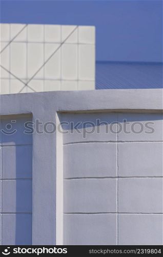 Abstract pattern of curve white concrete wall with blurred office building on blue sky background in vertical frame, architecture background design concept