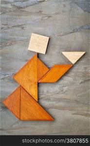 abstract picture of a figure offering a cup of tea or soup built from seven tangram wooden pieces against slate rock, a traditional Chinese puzzle game, the artwork copyright by the photographer