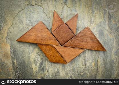 abstract picture of a flying bat built from seven tangram wooden pieces over a slate rock background, Halloween concept, artwork created by the photographer