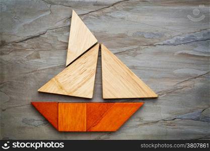 abstract picture of a sailing boat built from seven tangram wooden pieces over a slate rock background, travel or vacation concept, artwork created by the photographer