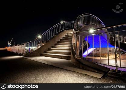 Abstract shapes and organic round lines of a public walking route along the harbor of Harlingen. Illuminated steps with LED and different colors yellow, purple and blue as a viaduct spanning for train tracks near the boulevard