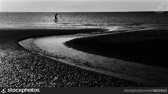 Abstract silhouette of tiny lonely man walking at seaside, lower head and sadness concept, beach with sand in curve