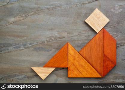 abstract sitting or relaxing figure built from seven tangram wooden pieces, a traditional Chinese puzzle game, slate rock background,artwork created by the photographer