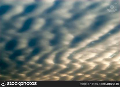 Abstract smooth gray and blue cloudscape with jagged wave forms and shadows, partly illuminated by sun behind clouds.