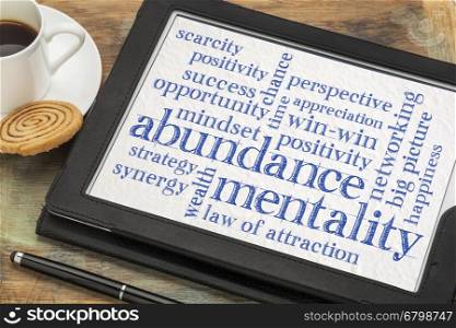 abundance mentality word cloud on a digital tablet with a cup of coffee