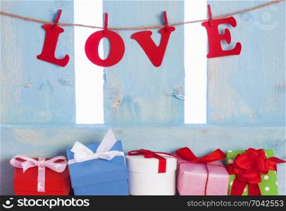 Abundance of colorful presents under a blue wooden fence and the word love spelled with red paper letters and tied to a string with wooden clips.
