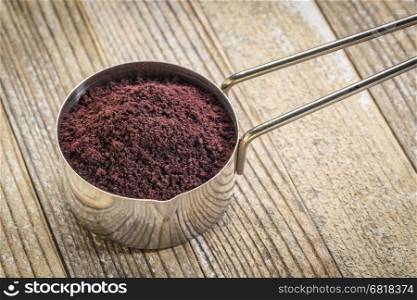 acai berry powder in a metal measuring scoop against grunge wood background