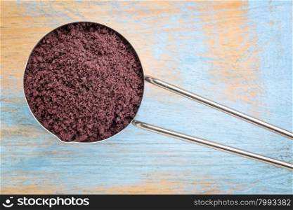 acai berry powder on a metal measuring scoop against painted grunge wood