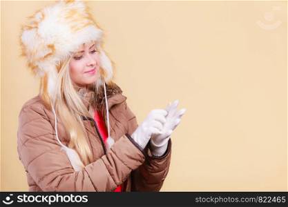 Accessories and clothes for cold days, fashion concept. Blonde woman in winter warm furry hat in russian style and jacket, looking at gloves.. Blonde woman in winter warm furry hat