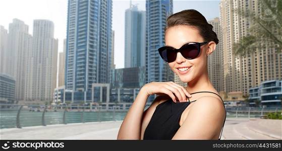 accessories, eyewear, fashion, people and luxury concept - beautiful young woman in elegant black sunglasses over dubai city street background