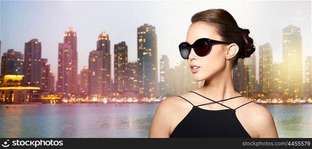 accessories, eyewear, fashion, people and luxury concept - beautiful young woman in elegant black sunglasses over night dubai city lights background