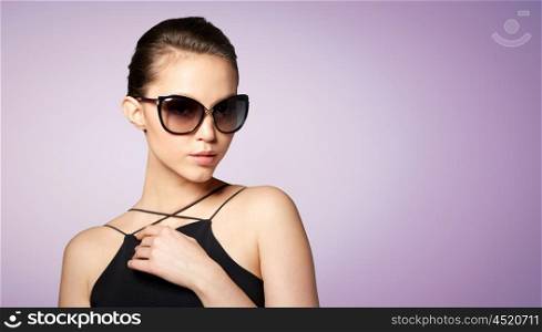 accessories, eyewear, fashion, people and luxury concept - beautiful young woman in elegant black sunglasses over violet background
