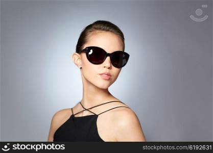 accessories, eyewear, fashion, people and luxury concept - beautiful young woman in elegant black sunglasses over gray background