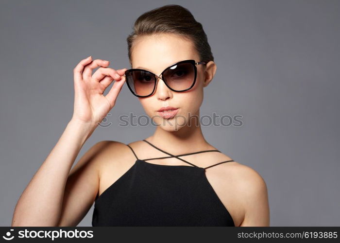 accessories, eyewear, fashion, people and luxury concept - beautiful young woman in elegant black sunglasses over gray background