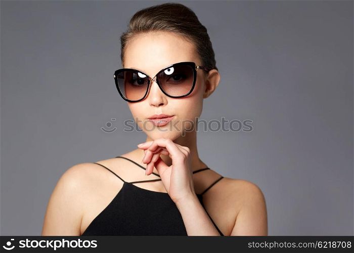 accessories, eyewear, fashion, people and luxury concept - beautiful young woman in elegant black sunglasses over gray background