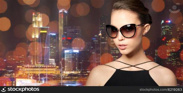 accessories, eyewear, fashion, people and luxury concept - beautiful young woman in elegant black sunglasses over night city lights background