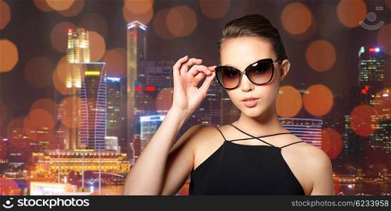accessories, eyewear, fashion, people and luxury concept - beautiful young woman in elegant black sunglasses over night city lights background