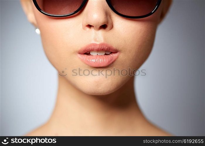 accessories, eyewear, fashion, people and luxury concept - close up of beautiful young woman in elegant black sunglasses over gray background