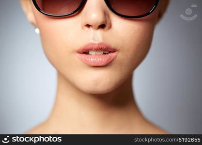 accessories, eyewear, fashion, people and luxury concept - close up of beautiful young woman in elegant black sunglasses over gray background