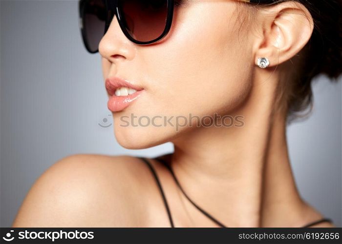 accessories, eyewear, fashion, people and luxury concept - close up of beautiful young woman in elegant black sunglasses over gray background