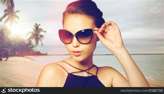 accessories, fashion, people and luxury concept - beautiful young woman in elegant black sunglasses over exotic tropical beach with palm trees background. beautiful young woman in elegant black sunglasses