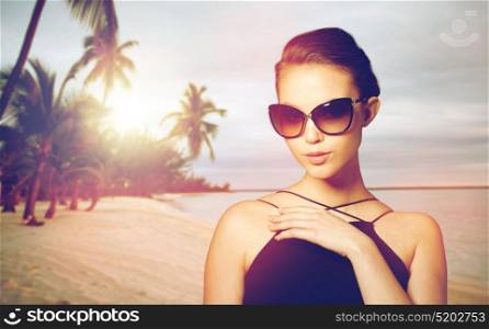 accessories, fashion, people and luxury concept - beautiful young woman in elegant black sunglasses over exotic tropical beach with palm trees background. beautiful young woman in elegant black sunglasses