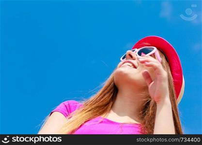 Accessories, female summer fashion, sun protection concept. Smiling beautiful woman wearing heart shaped sunglasses and red hat looking at sky, outdoor shot on sunny day.. Woman wearing heart shaped sunglasses and hat