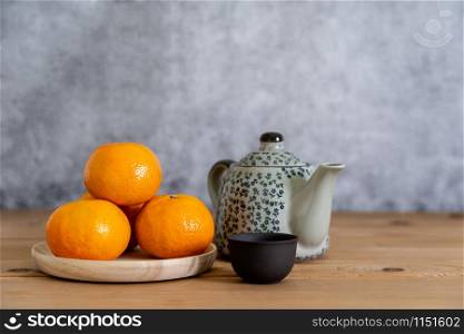 Accessories on Lunar New Year & Chinese New Year vacation concept holiday background.Orange in wood basket with gold money and red packet & white plum blossom on brown & grey stone backdrop.