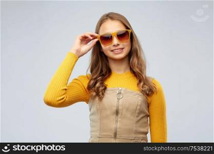 accessory, eyewear and fashion concept - smiling young teenage girl in sunglasses over grey background. smiling young teenage girl in sunglasses