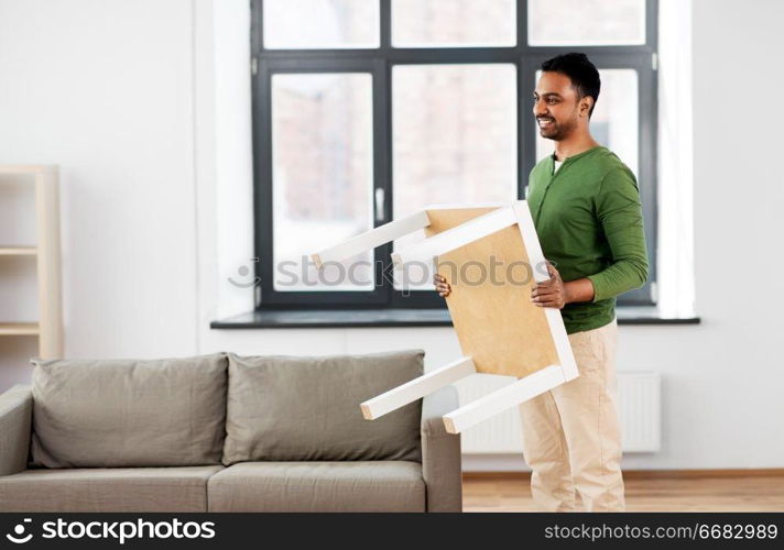 accommodation, furniture and interior concept - happy indian man holding coffee table at home. happy indian man holding coffee table at home