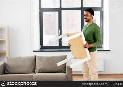 accommodation, furniture and interior concept - happy indian man holding coffee table at home. happy indian man holding coffee table at home