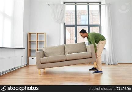 accommodation, furniture and interior concept - happy indian man moving sofa at home. happy indian man moving sofa at home