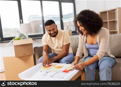 accommodation, moving and real estate concept - happy african american couple with blueprint and color palettes at new home. couple with blueprint and color palettes at home