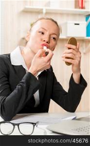 Accountant paints her lips at a desk and looking into a small mirror