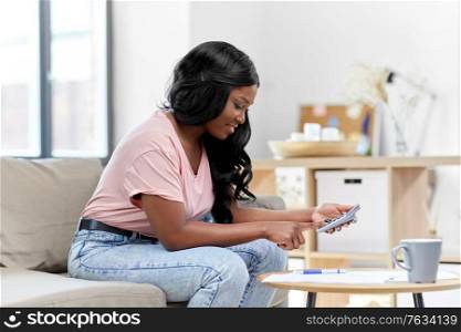 accounting, taxes and finances concept - happy smiling young african american woman with papers and calculator at home. african woman with papers and calculator at home