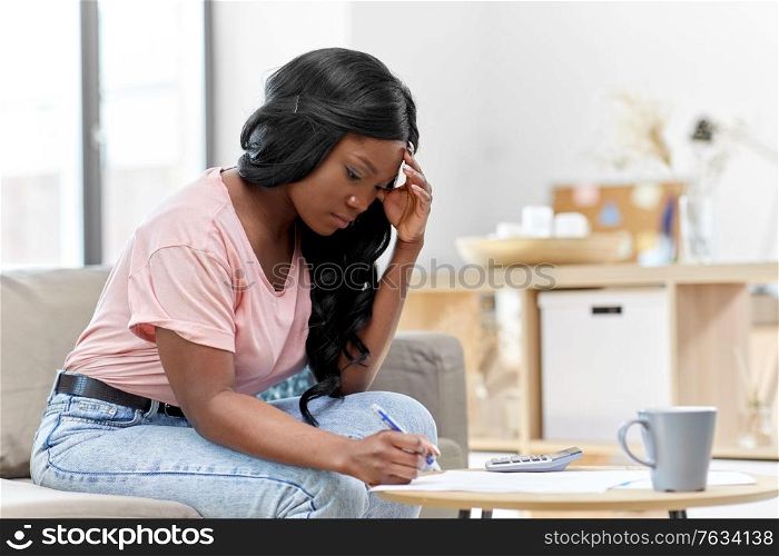 accounting, taxes and finances concept - young african american woman with papers and calculator at home. african woman with papers and calculator at home