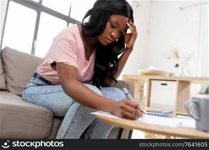 accounting, taxes and finances concept - young african american woman with papers at home. african woman with papers at home