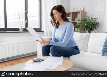 accounting, taxes and finances concept - young woman with papers and calculator at home. woman with papers and calculator at home
