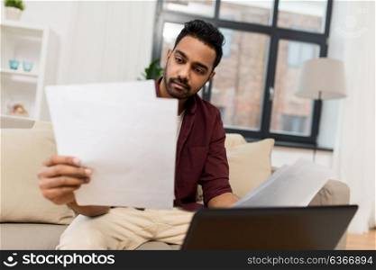 accounting, technology and people concept - man with laptop computer and papers at home. upset man with laptop and papers at home