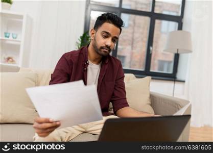 accounting, technology and people concept - upset man with laptop computer and papers at home. upset man with laptop and papers at home